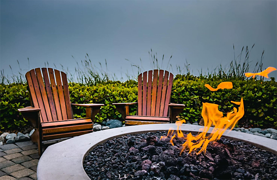 two Adirondack chairs at a circular stone fireplace with a dancing flame.